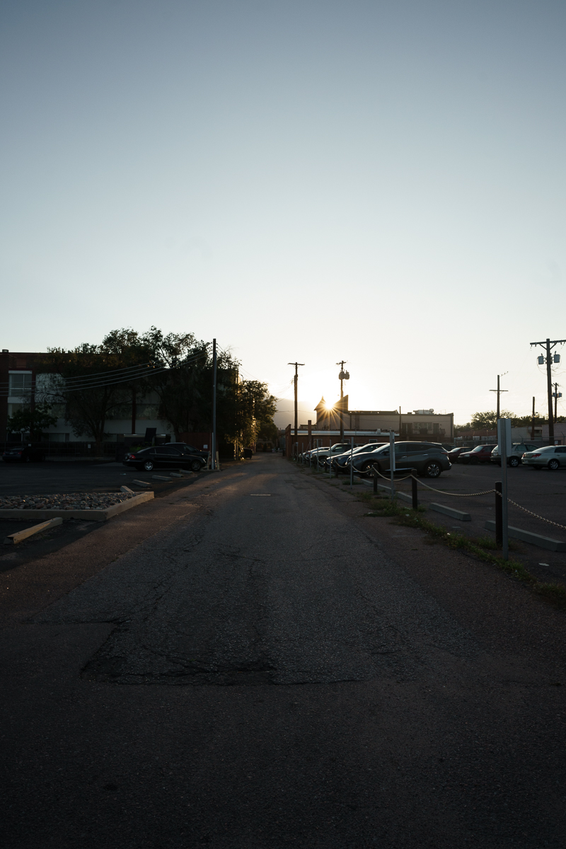 picture of an empty alley with the sun shining past the top of a building just before sunset